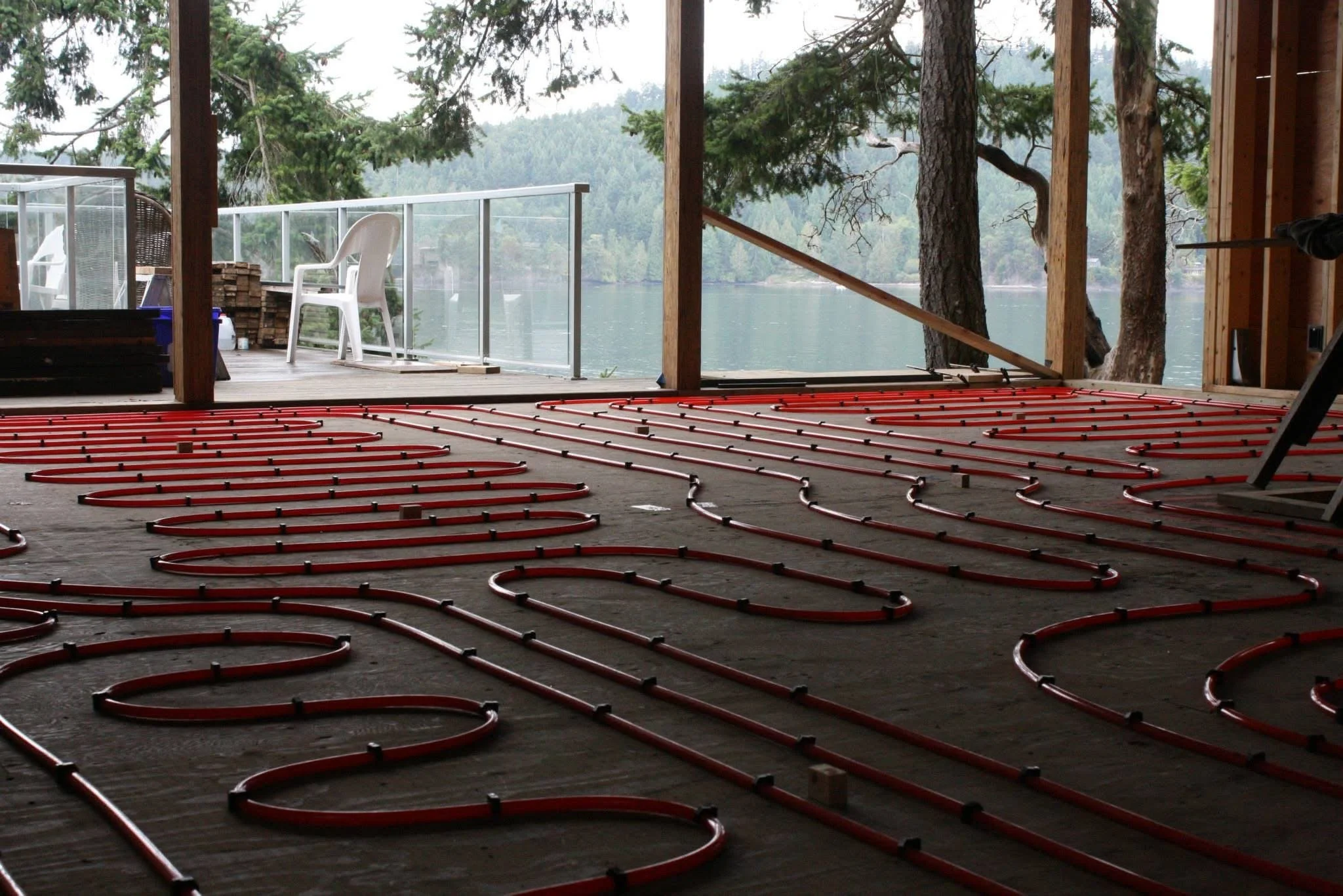 Installation of radiant floor heating with red tubing inside a house overlooking a lake with trees in the background.