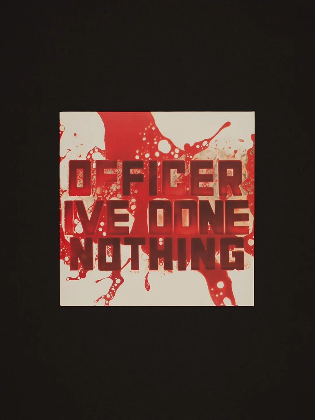Square sign with red and white background, splattered with red paint, displaying the text 'OFFICER WE DONE NOTHING' in bold red letters.