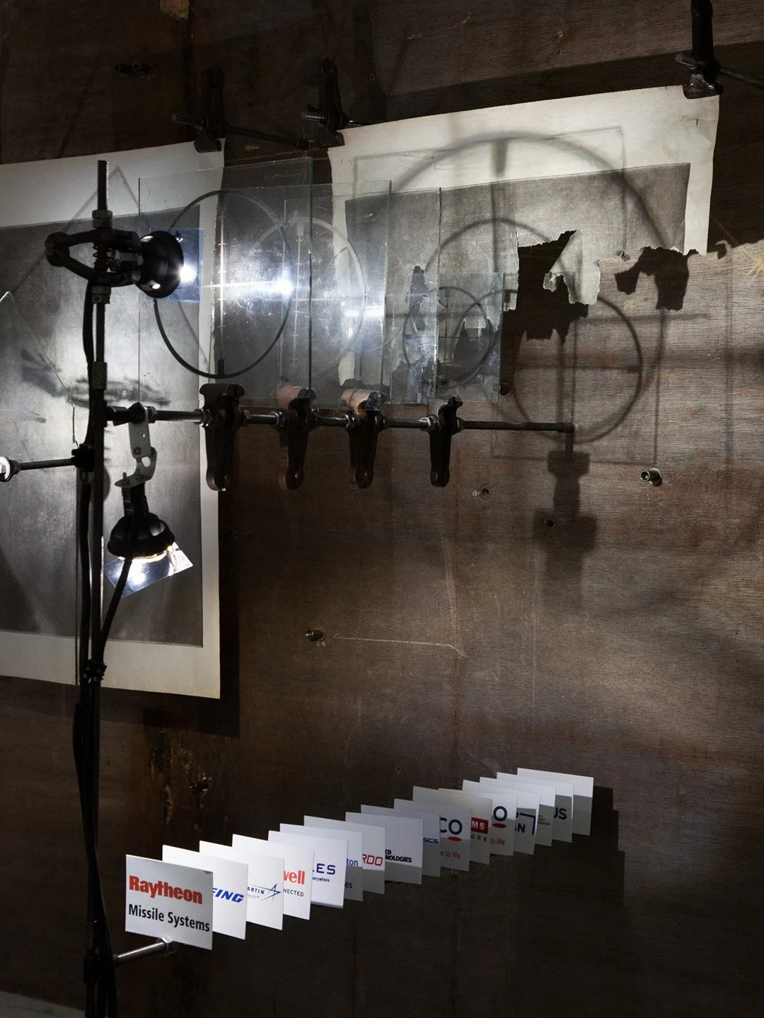 Display of missile systems with labeled cards, light source, and transparent shields on a dark wooden wall.