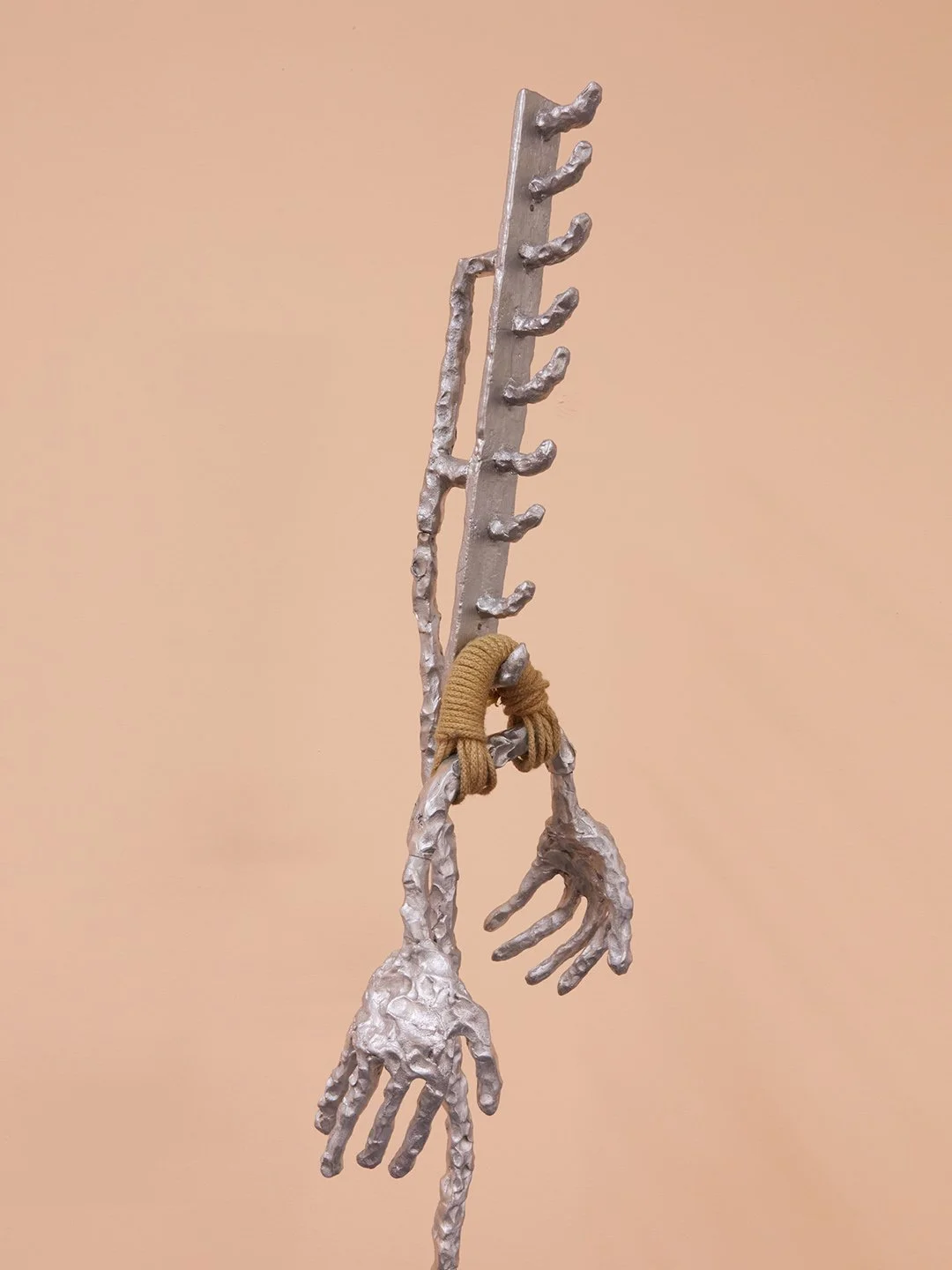 Art sculpture resembling a knife with two skeletal hands attached by brown rope, set against a neutral background.