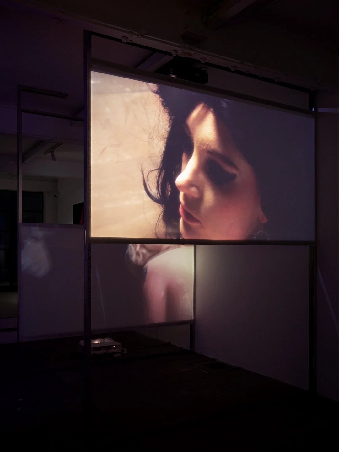 Projected image of a woman's face with dark hair and makeup, captured in a moody, artistic style.