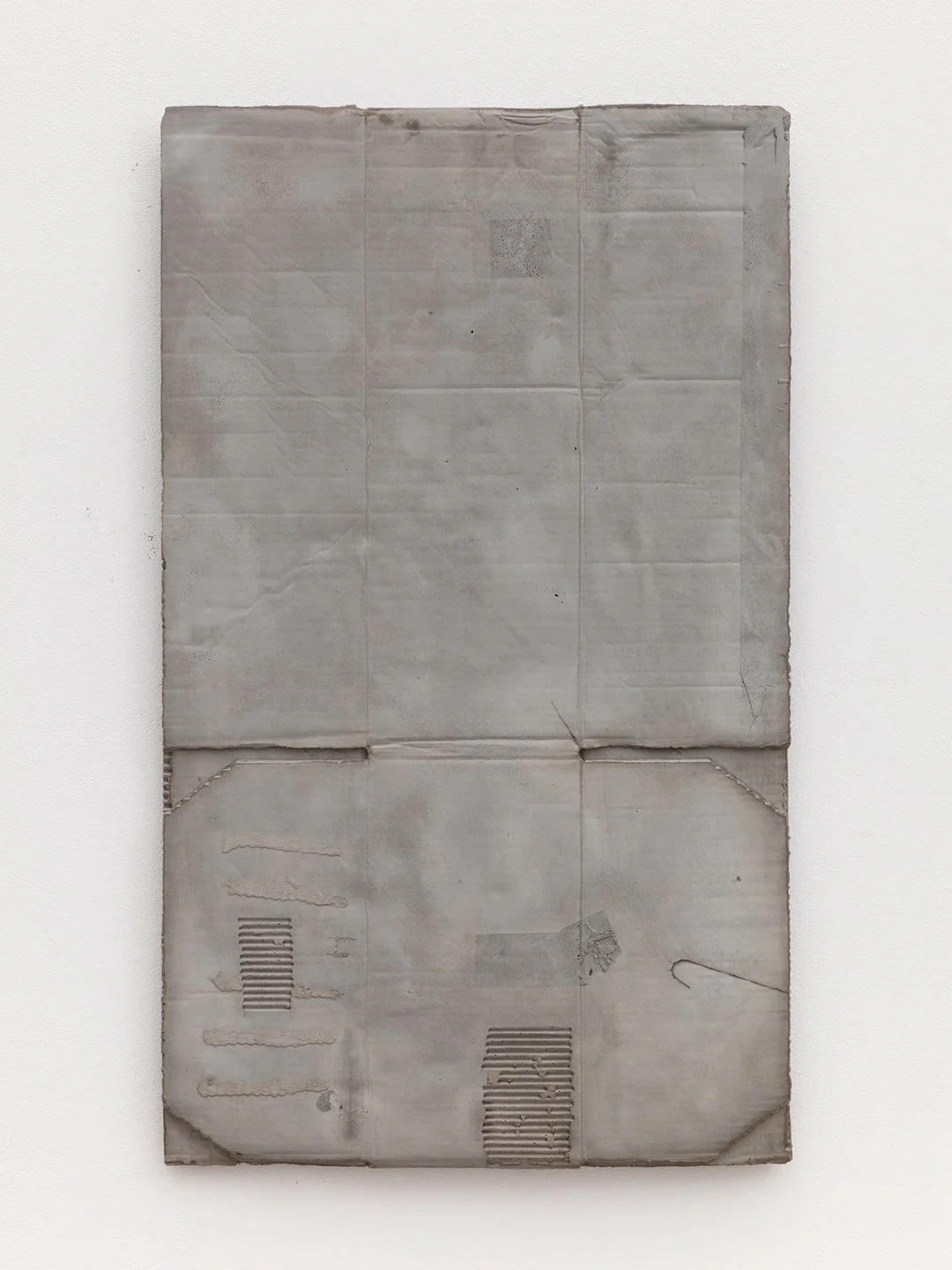 A worn, crumpled gray paper with tape and perforation marks, mounted on a white wall.