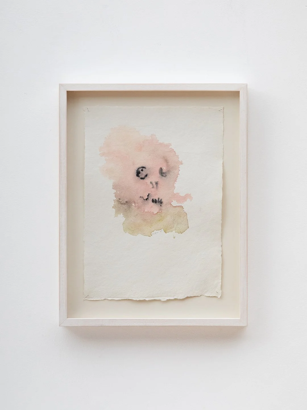 Watercolor painting of an abstract face on textured paper, displayed in a light wooden frame.