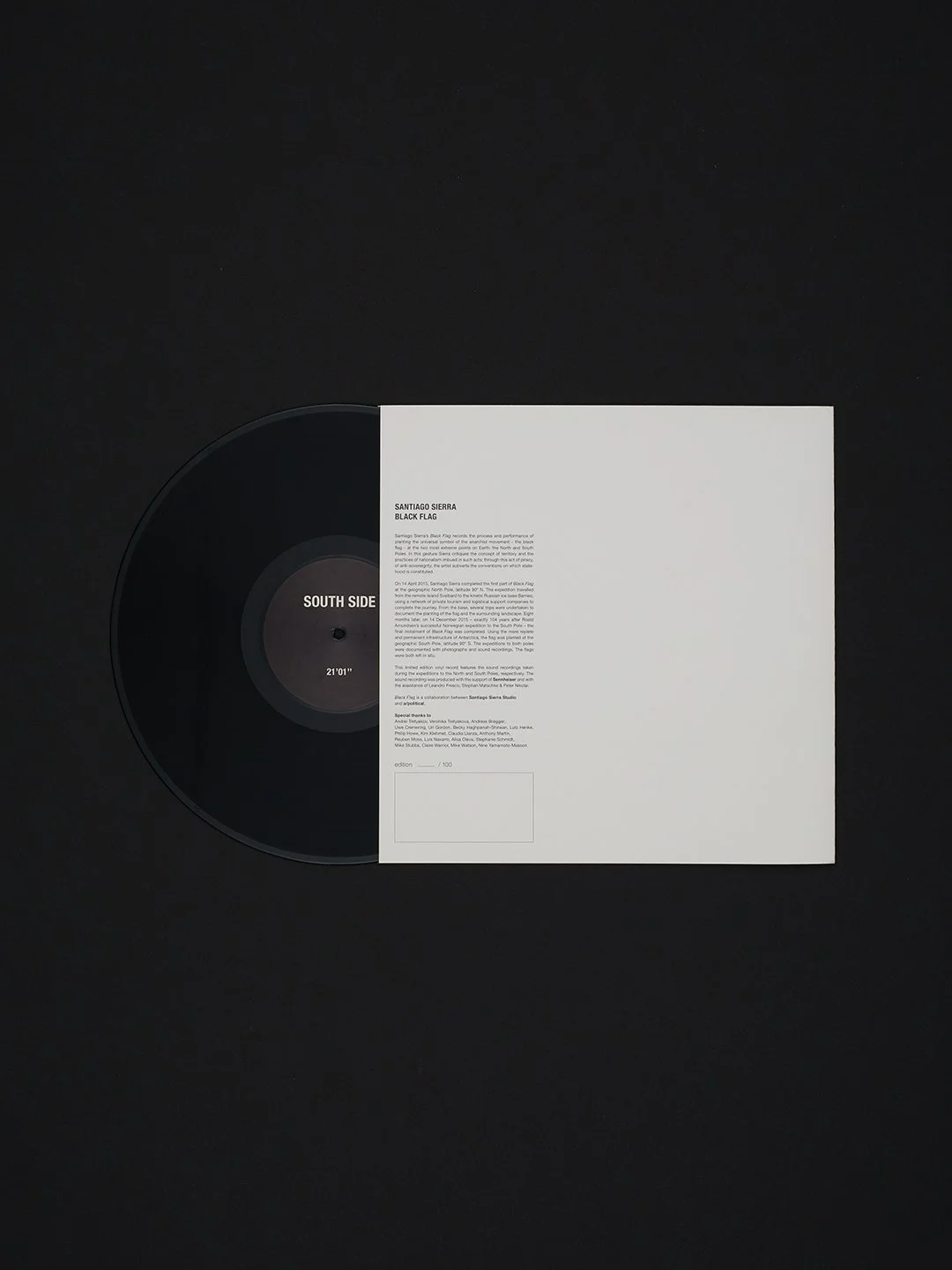 Black vinyl record partially covered by white booklet with text, on a black background.