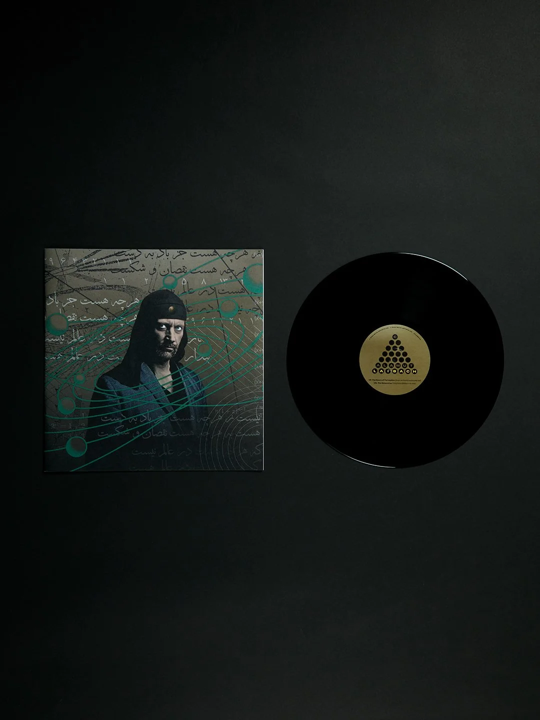A vinyl record and its album cover on a black background. The album cover features a man with a beard wearing a dark hoodie, with scientific and handwritten elements in the background.