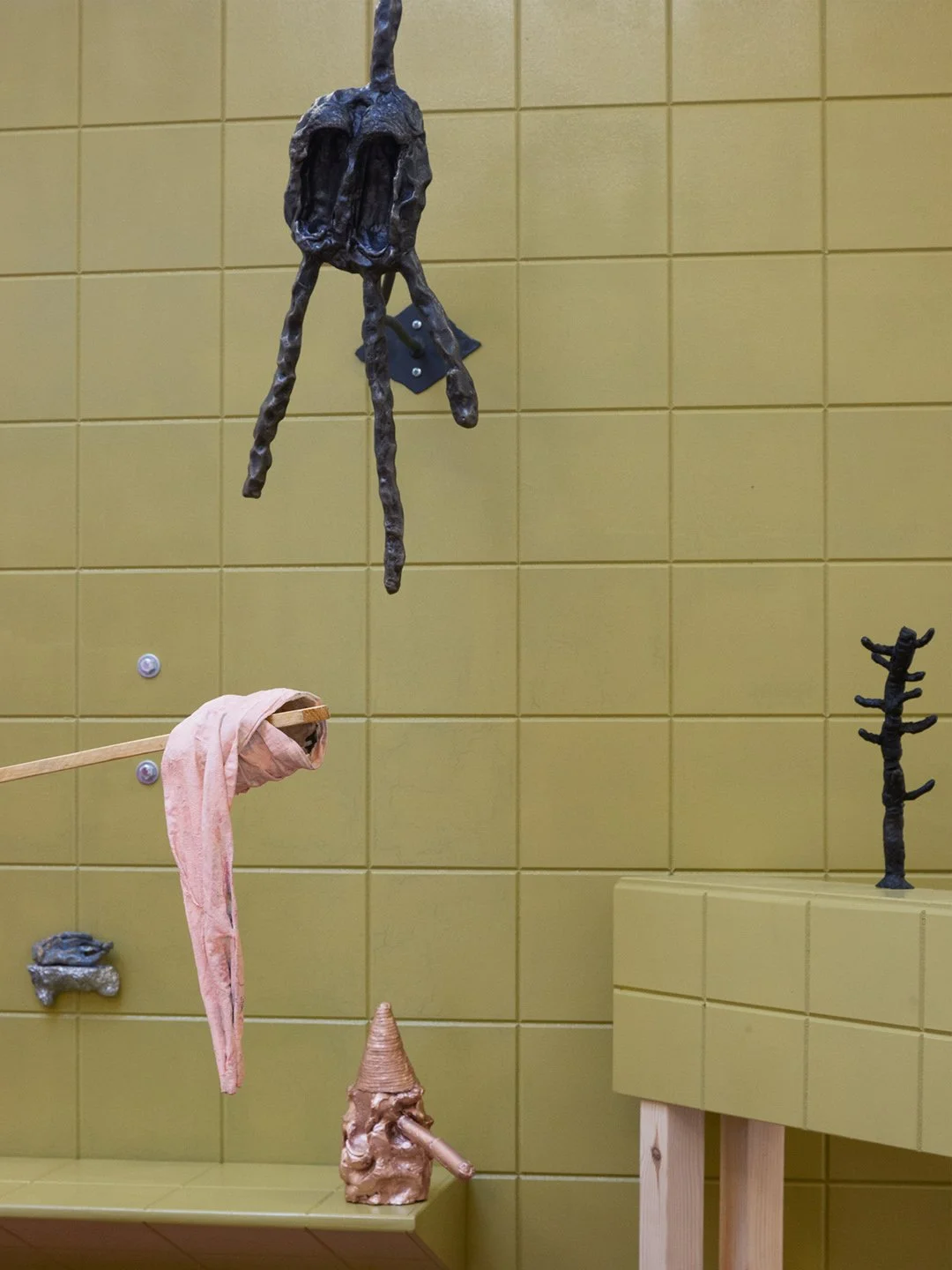 Art installation featuring various small sculptures and objects on a yellow-tiled wall and surface.
