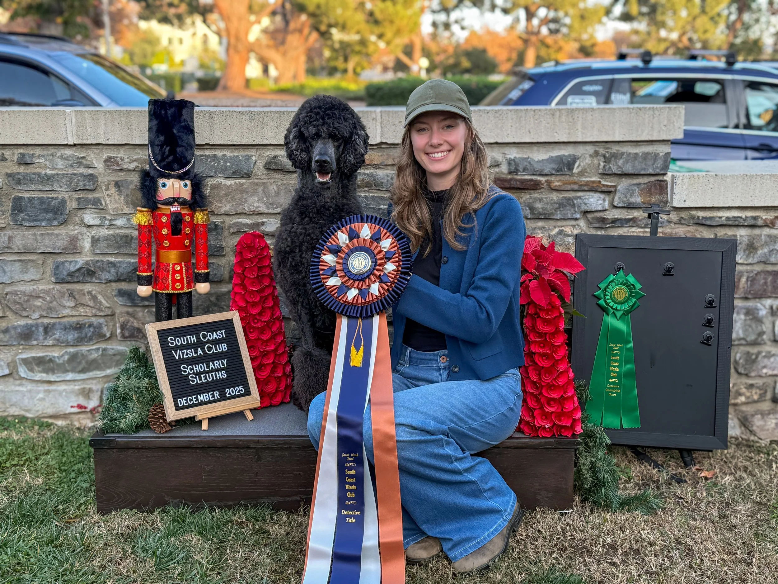 Standard poodle and dog trainer sitting with their AKC Detective title ribbon