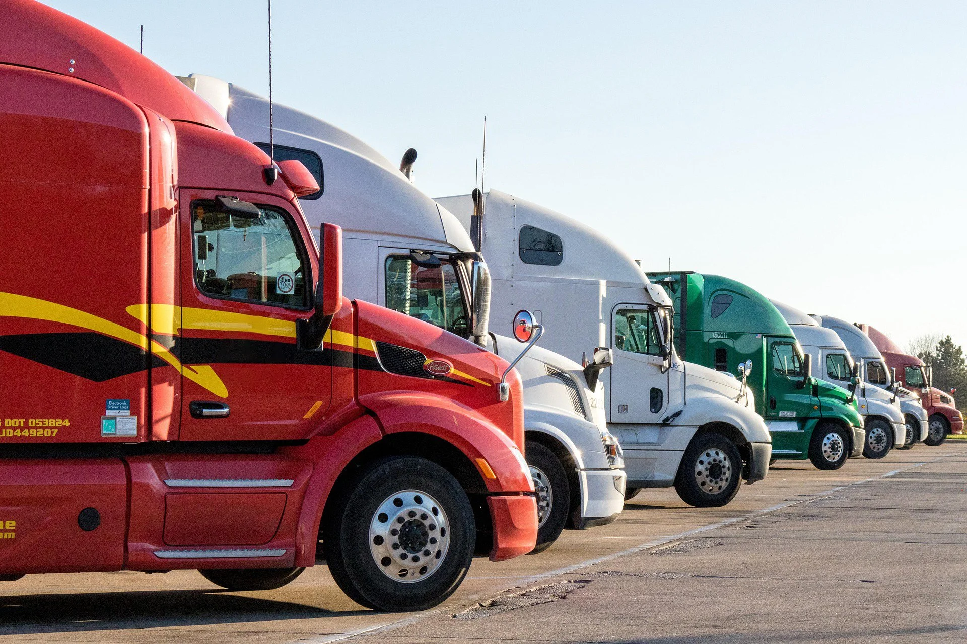 Line of various colored semi-trucks parked in a lot under a clear sky.