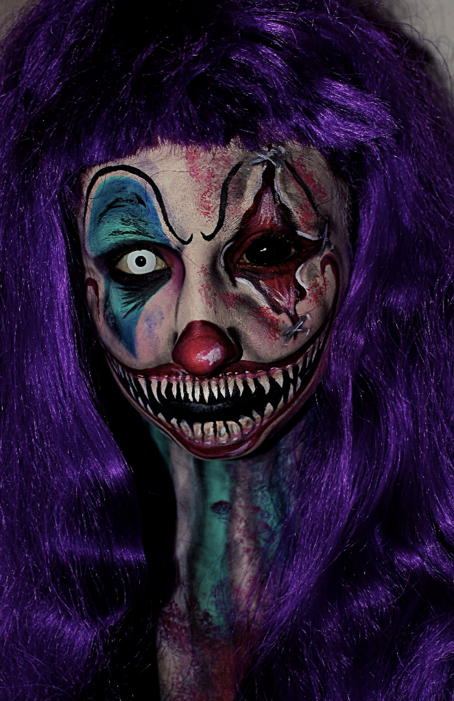 Person with clown makeup, purple wig, and eerie black and white face paint with sharp teeth design.