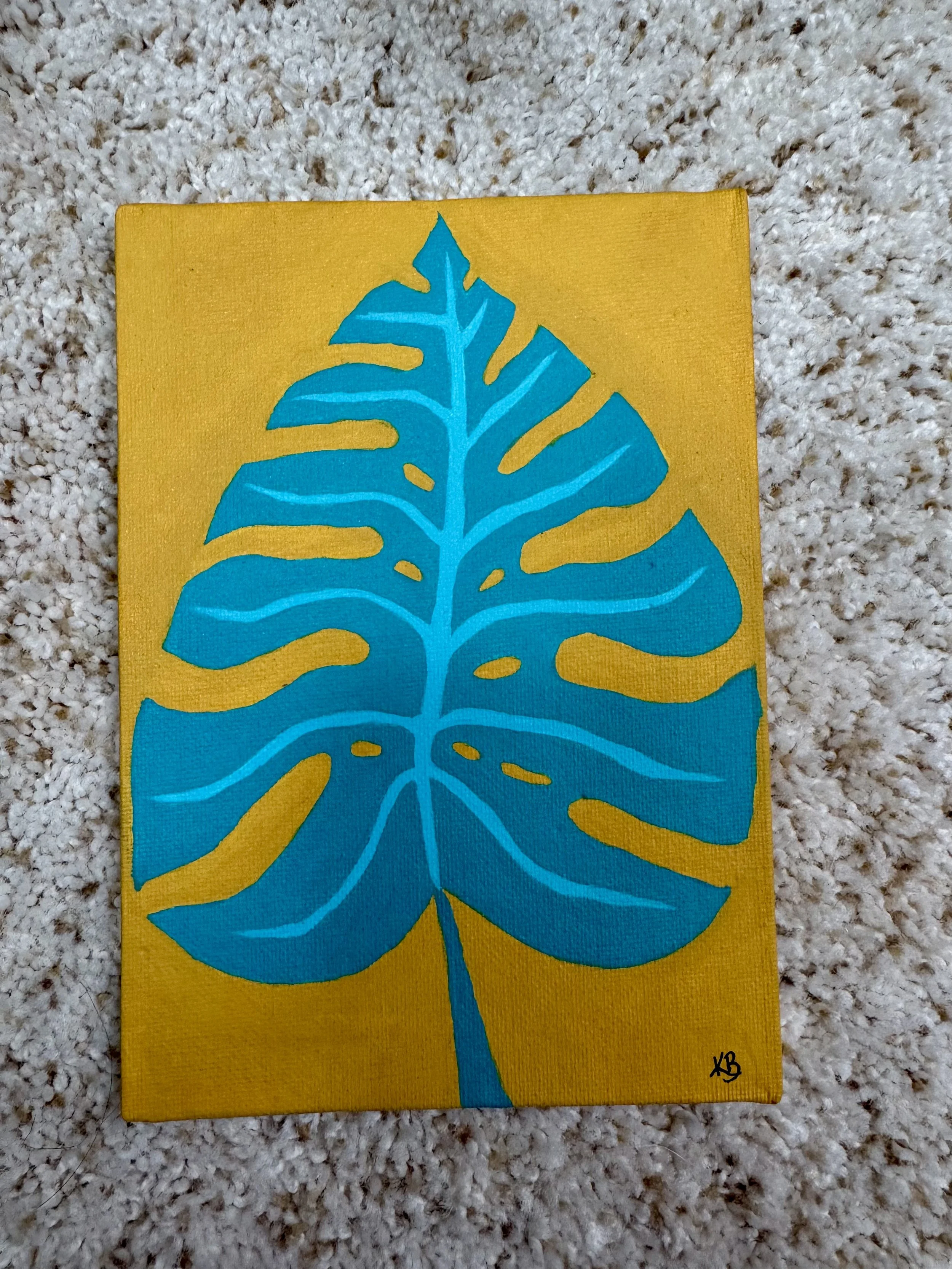 A painting of a large blue monstera leaf on a yellow background, signed 'KB' in the bottom right corner.
