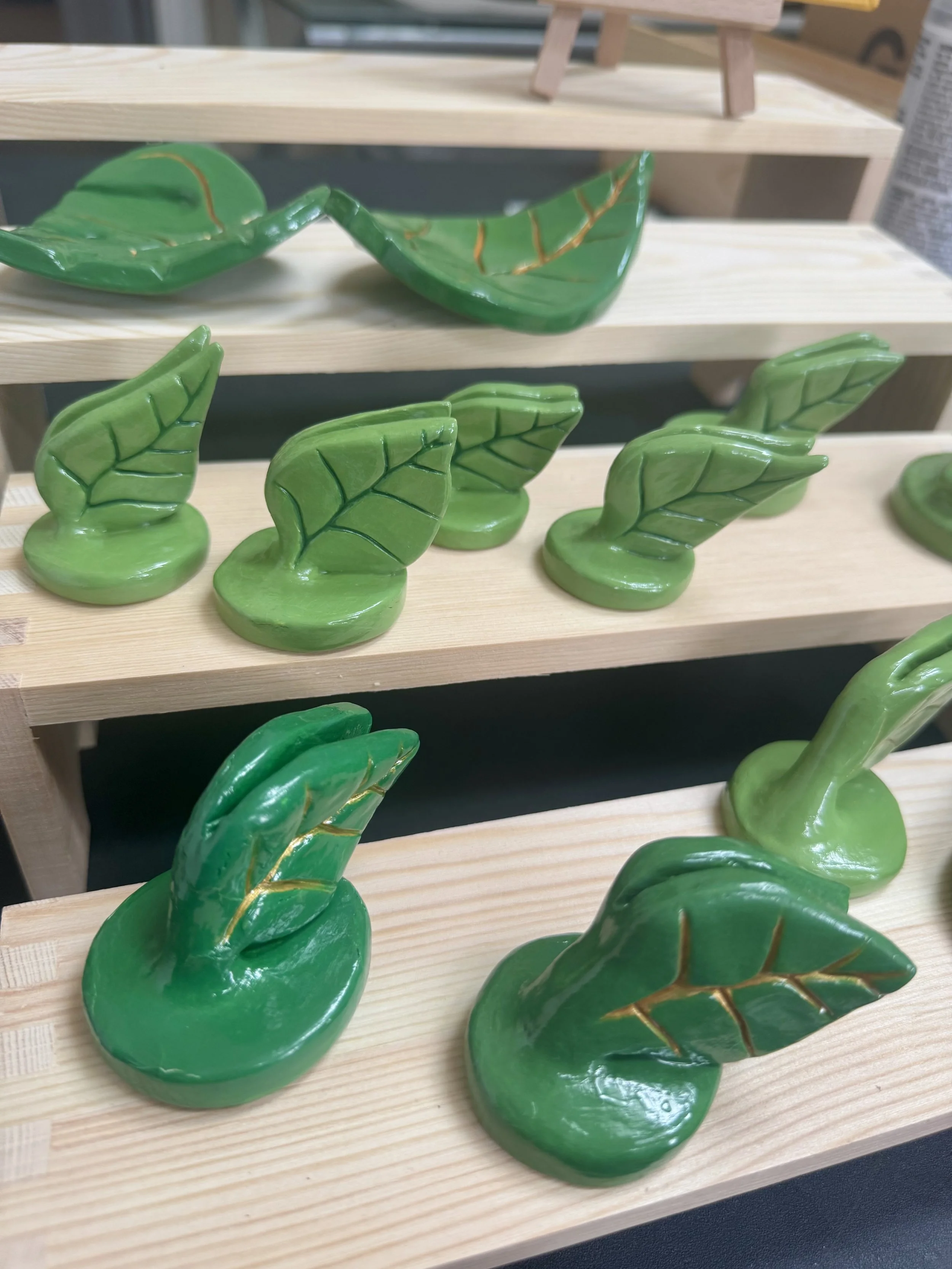 Green ceramic leaf figurines displayed on wooden shelves.