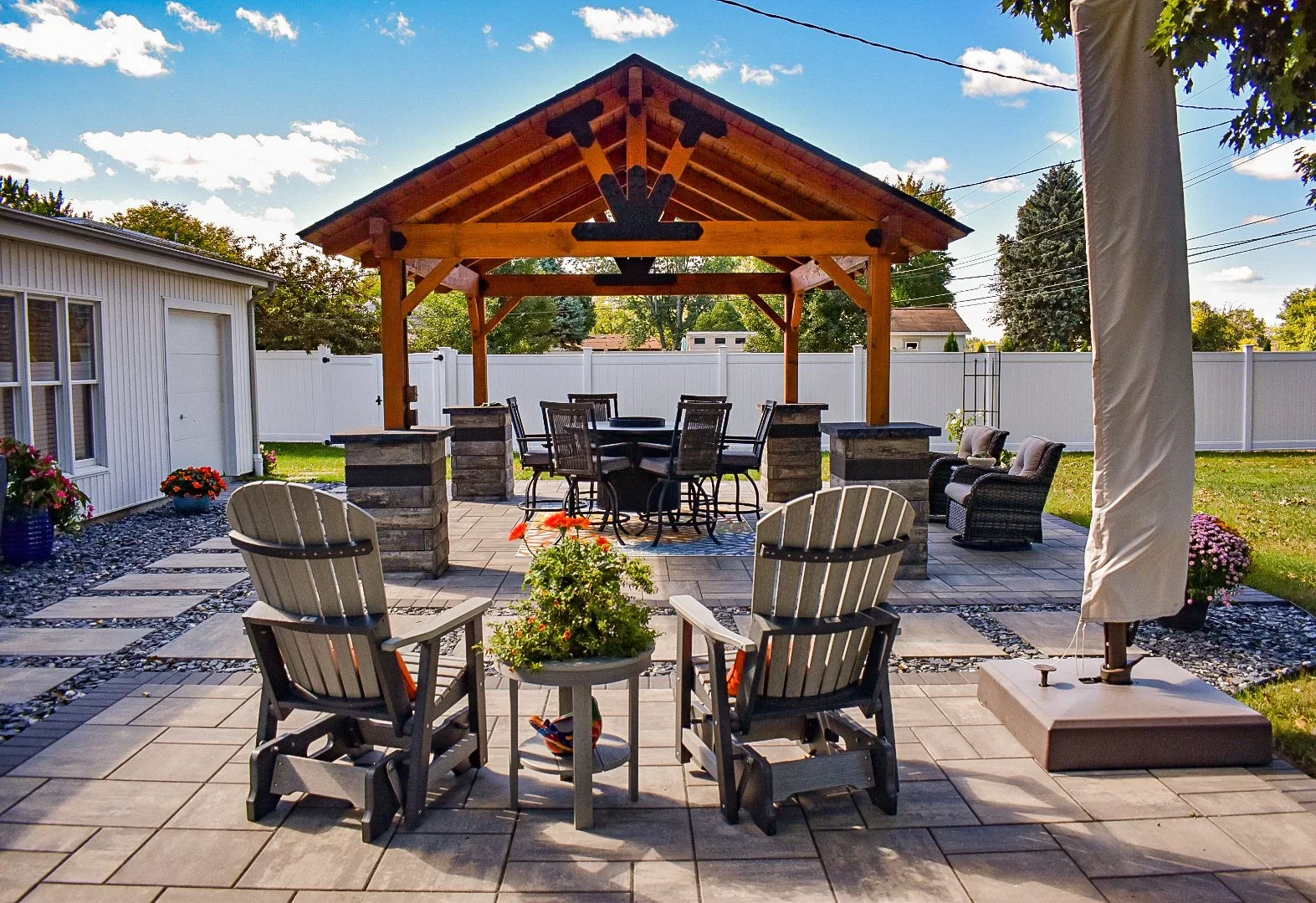 A custom paver patio with wooden pavilion, outdoor dining area, and seating space in Flat Rock, MI featuring outdoor living design