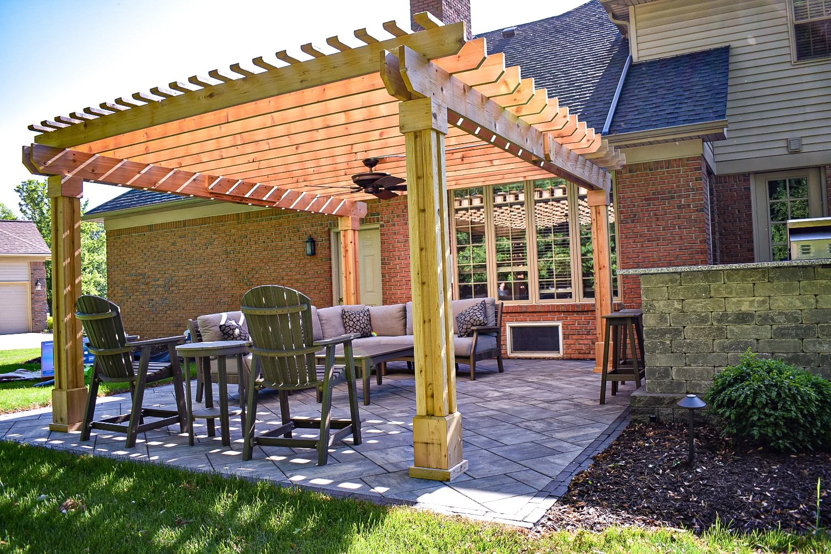 Backyard patio with a wooden pergola, outdoor furniture, and a brick house in the background.