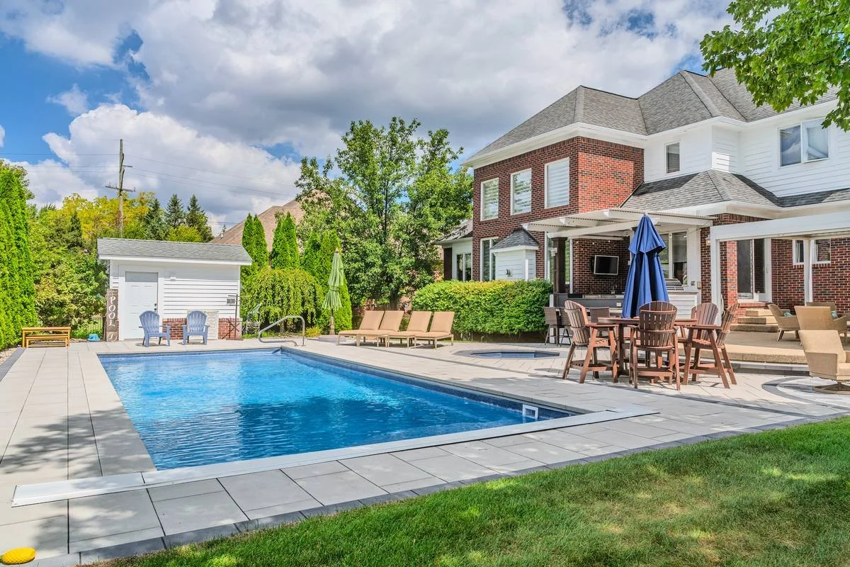 Rectangular pool with paver deck, patio dining set and lounge chairs beside a two-story home — GLC Landscaping & Pools