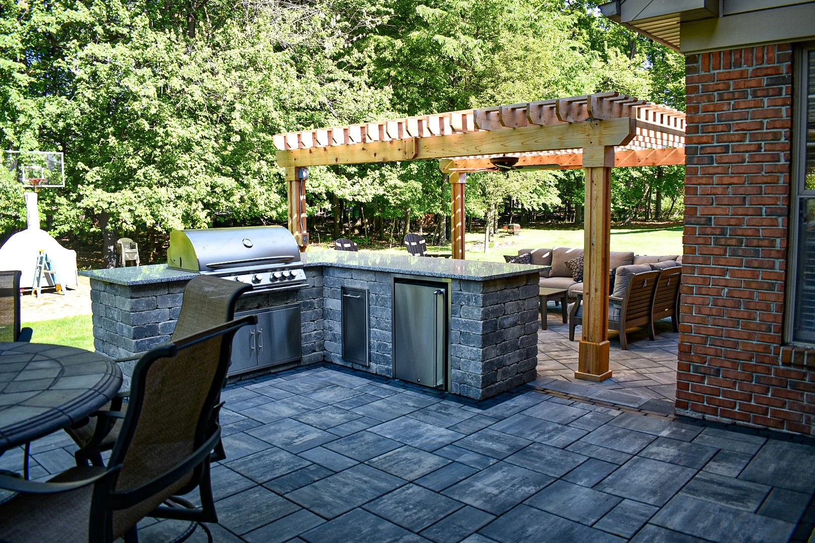 Backyard patio with outdoor kitchen and seating area, surrounded by trees.