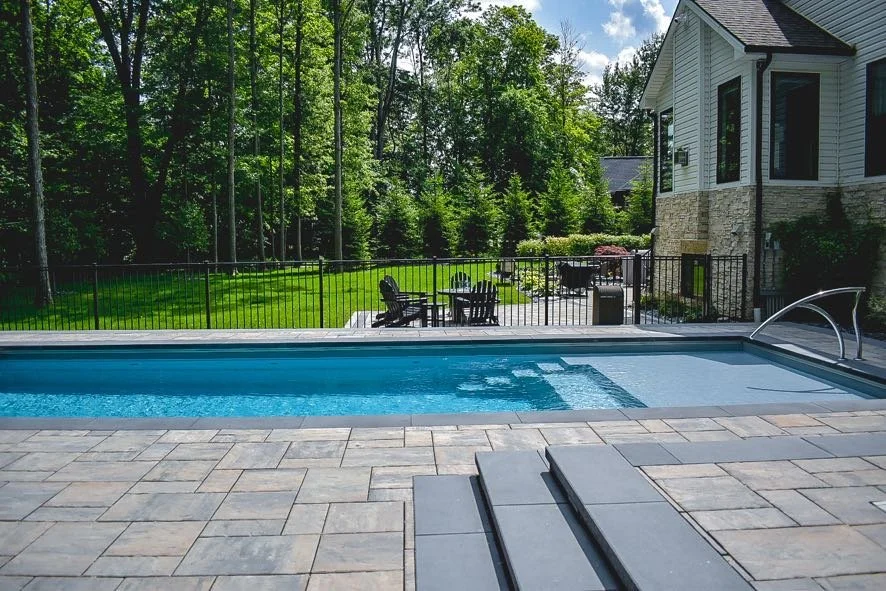 Backyard with a swimming pool, patio furniture, and a house surrounded by trees.
