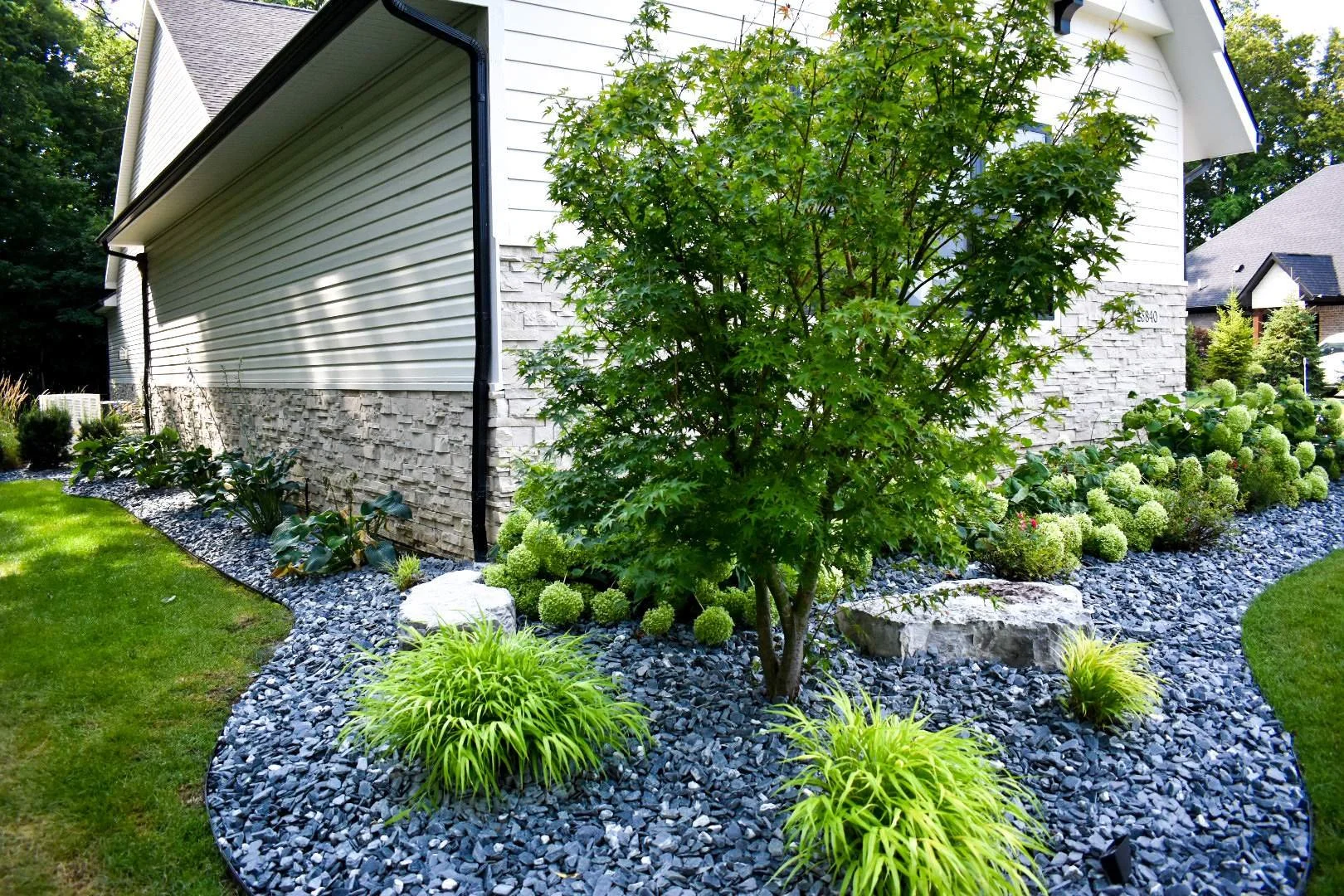 Front yard landscaping with planting beds, decorative stone, and landscape lighting enhancing curb appeal in Woodhaven, MI