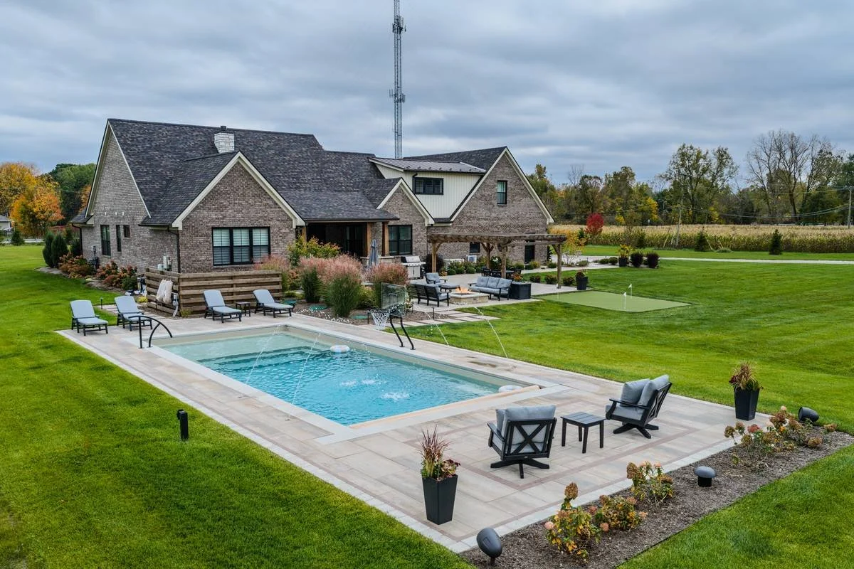 Inground pool with deck jets, paver patio, lounge chairs and putting green beside a brick home — GLC Landscaping & Pools