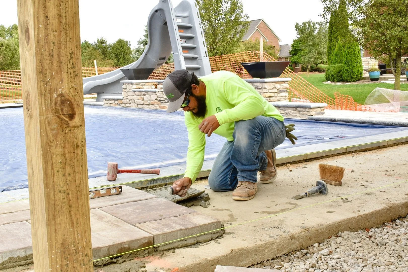 Paver patio installation in progress with contractor laying brick paving around pool area in Canton, MI