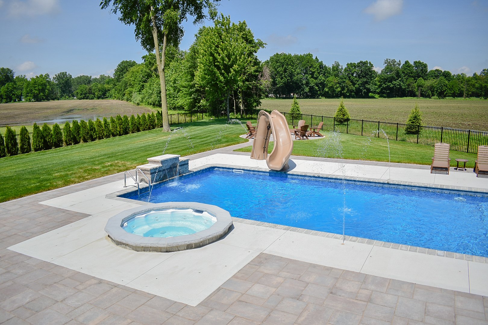 Backyard entertainment space planning combining a pool, integrated spa, fire pit, and expansive patio design — GLC Lawn & Landscape