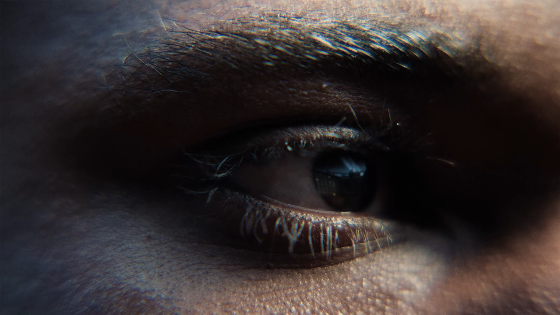 Close-up of a person's eye with dark skin, showing detailed eyelashes, eyelid, and eyebrow.