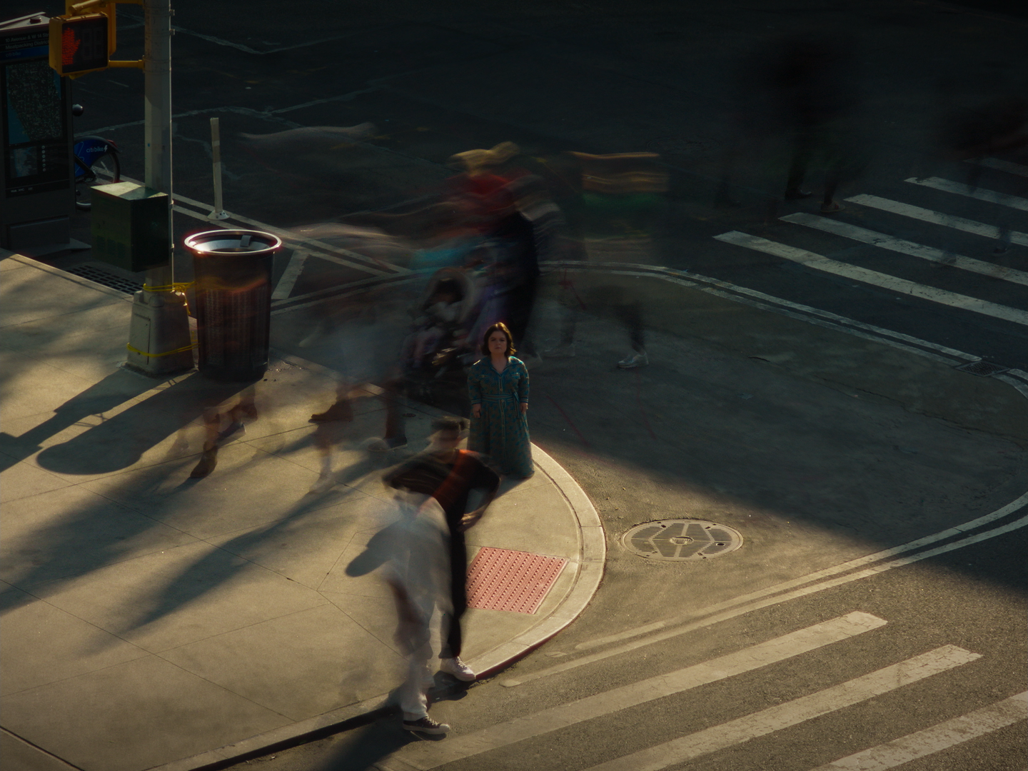 A woman standing at a busy city crosswalk with blurry motion of pedestrians passing by during daylight.