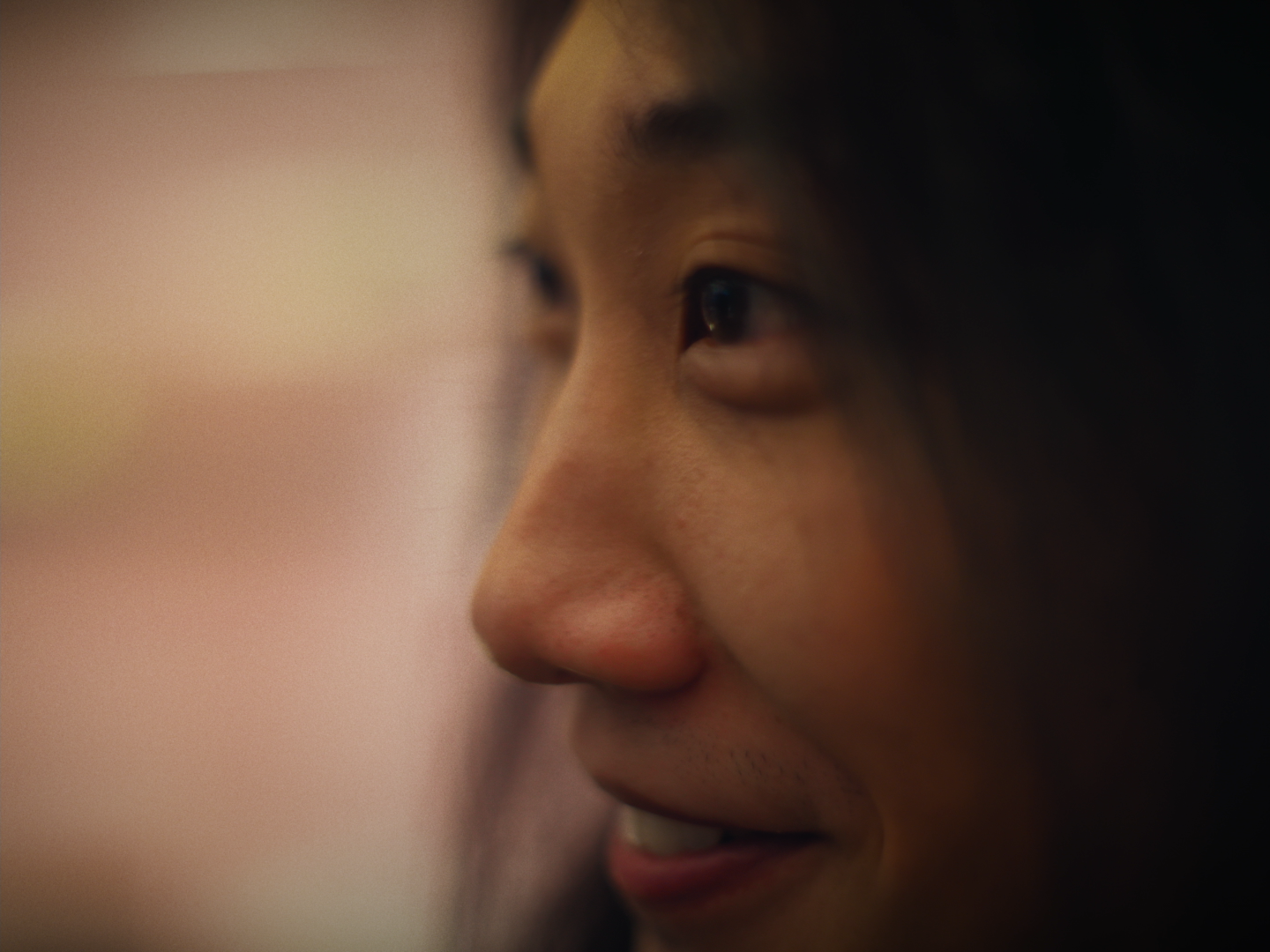 Close-up of a young woman's face, smiling, with focus on her right eye and nose, softer background.