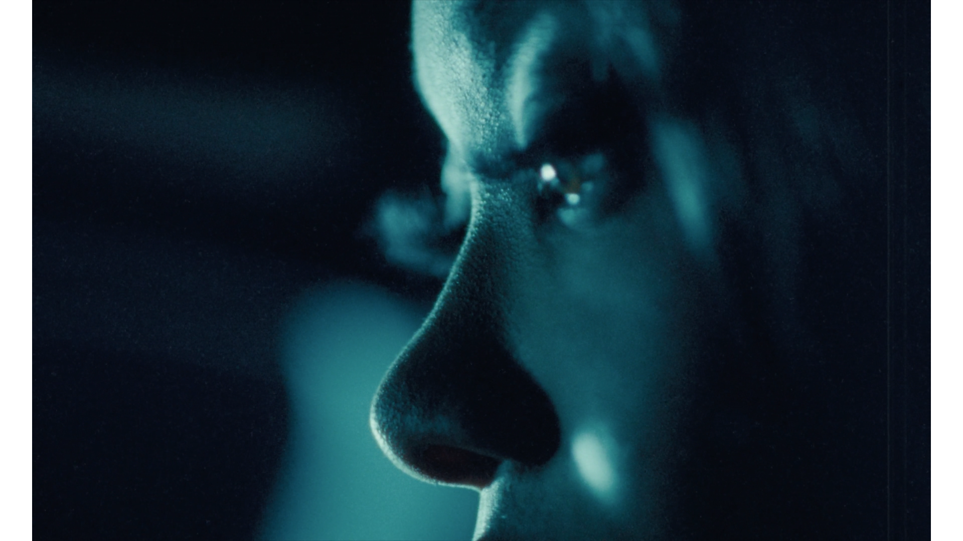 Close-up of a person's face in profile with focus on the nose and eye, shrouded in dark lighting.
