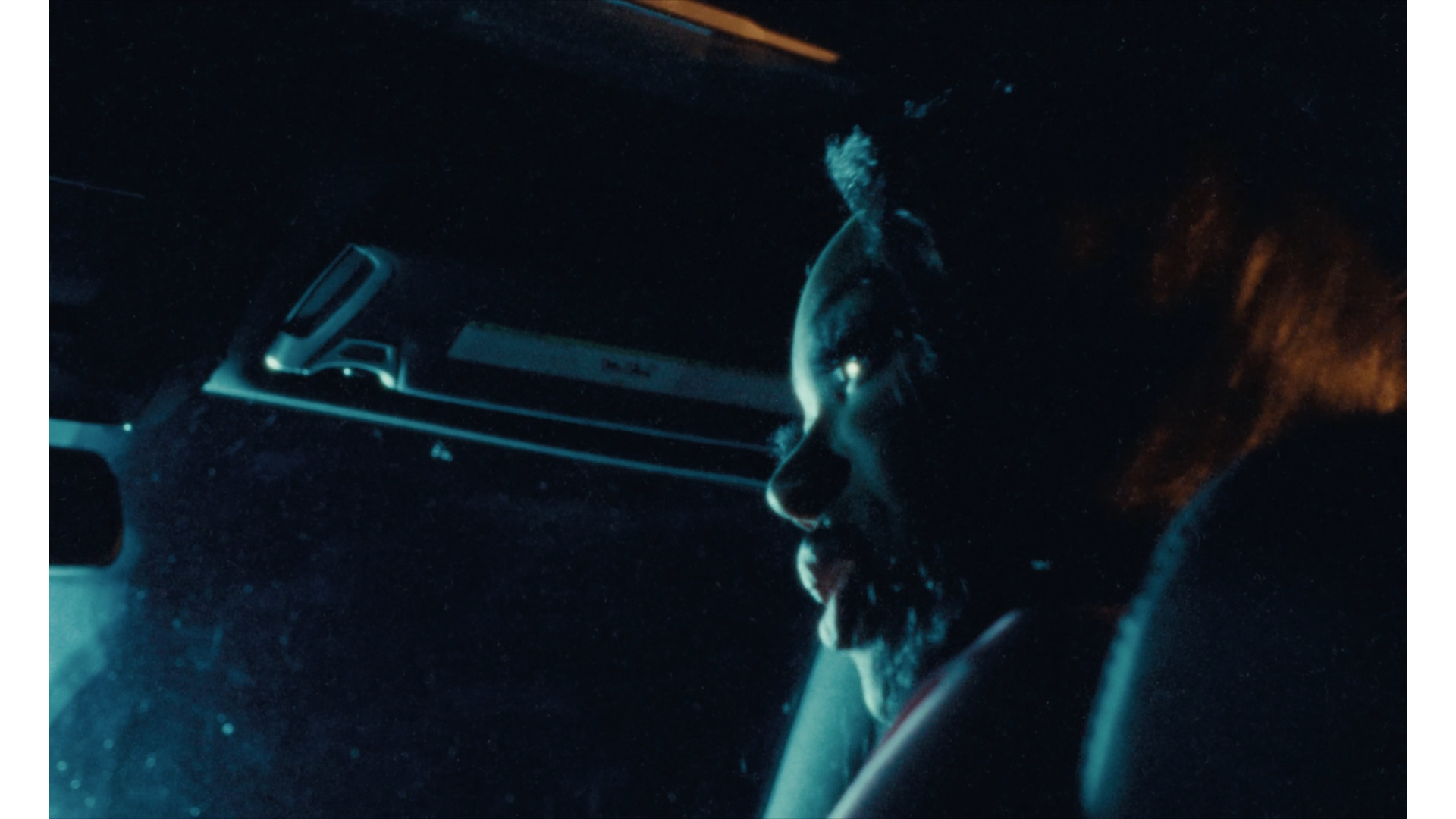 A young woman with curly hair and wearing large earrings is sitting inside a car at night, illuminated by the dashboard lights.