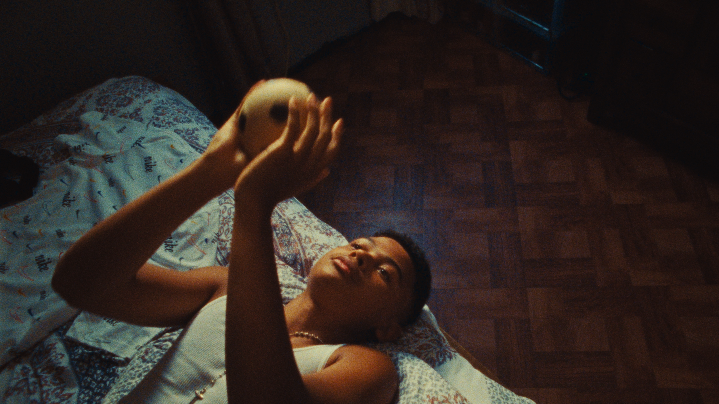 A young person lying on a bed with floral and patterned bedsheets, holding a white object, possibly a ball or decoration, in their hands and looking at it.