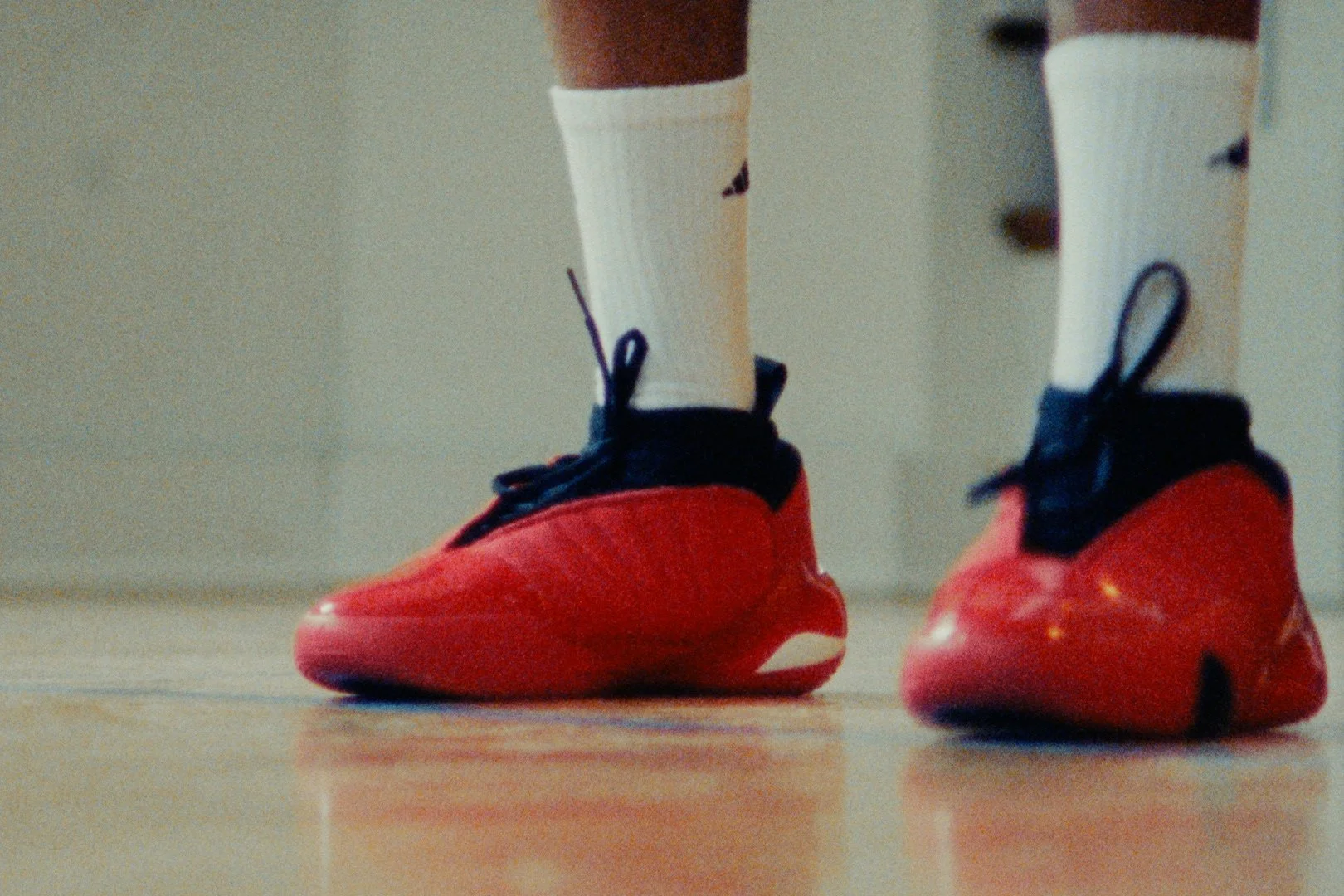 Close-up of a person wearing yellowish-white athletic socks and red sports shoes standing on a wooden floor.