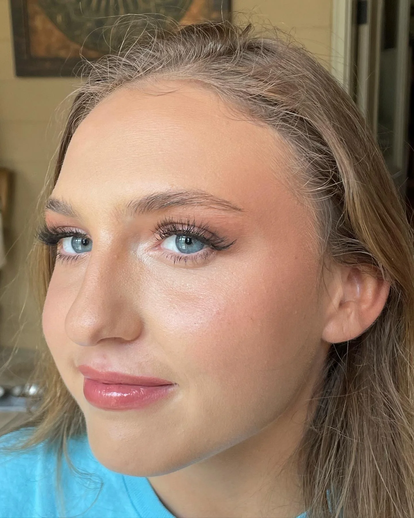 Close-up of a woman with blue eyes, styled makeup, and light brown hair, wearing a light blue top.