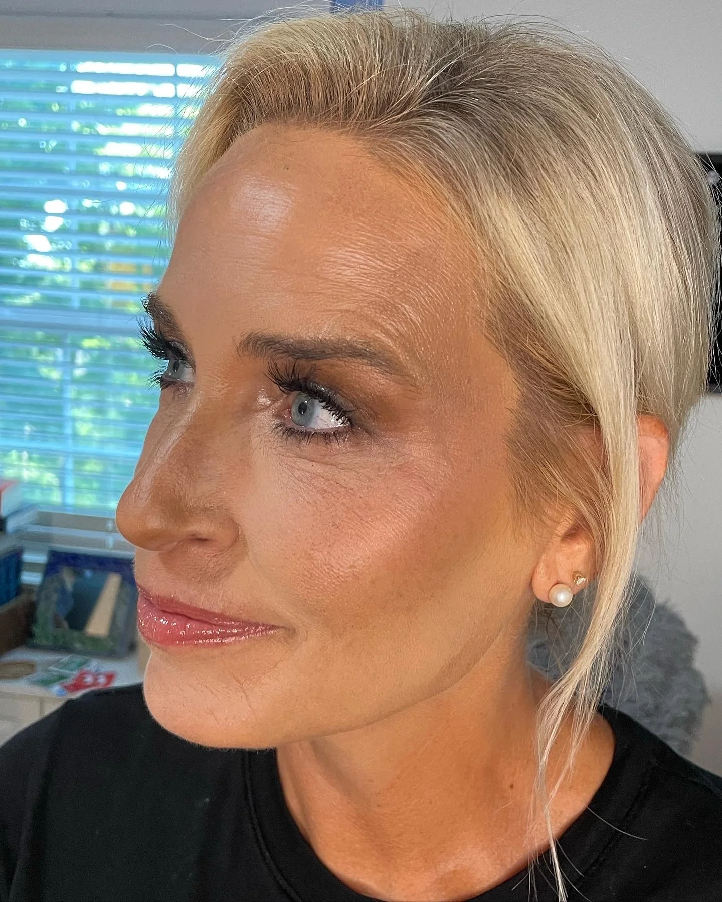 Close-up of a woman with blonde hair, blue eyes, wearing pearl earrings, with makeup, looking to her right.