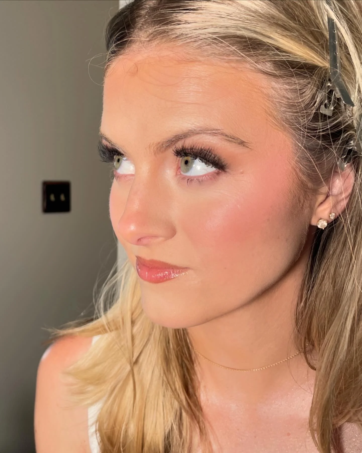 A woman with blonde hair, wearing earrings and a thin necklace, looking to her left with a soft smile and natural makeup.