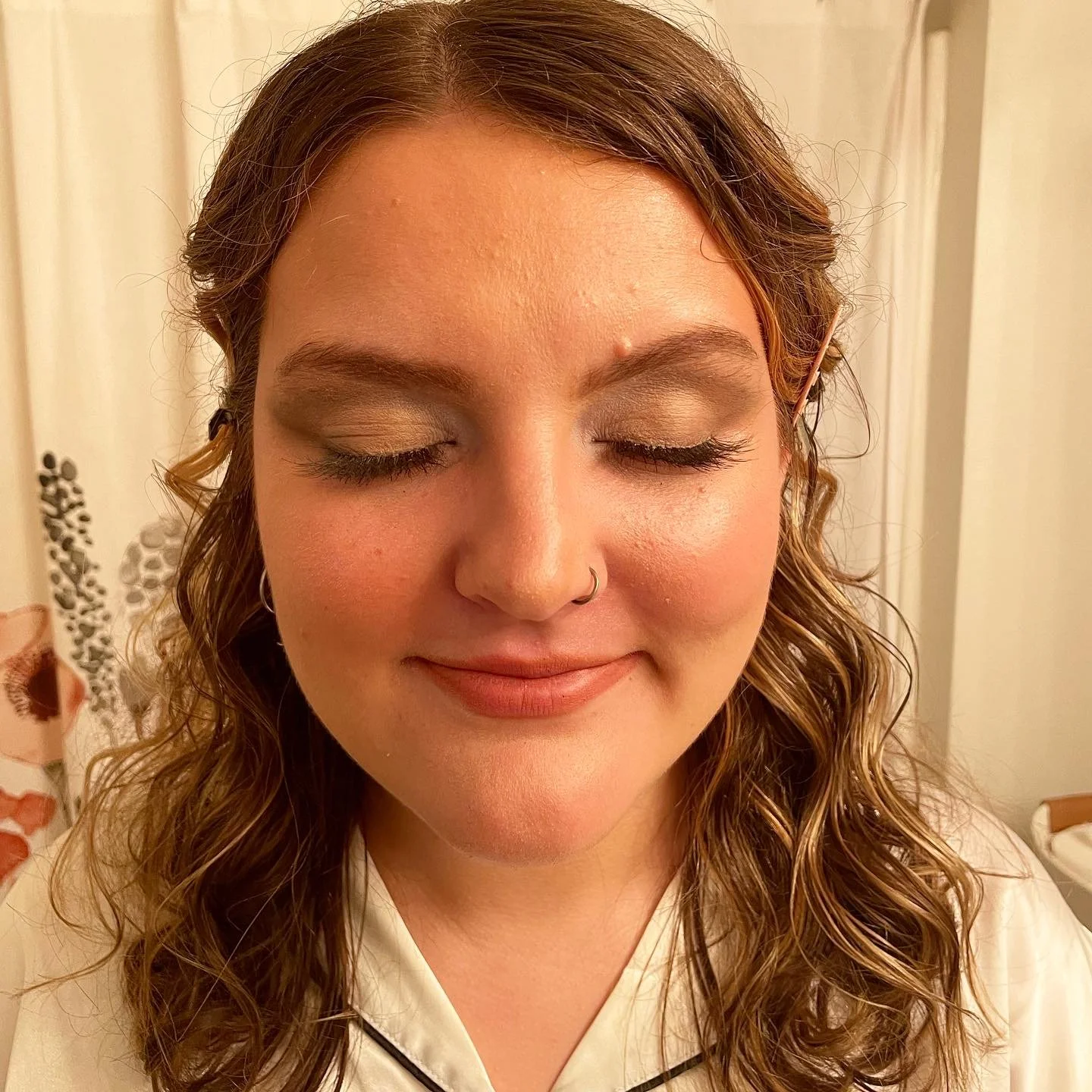 A woman with curly hair, closed eyes, and wearing makeup, smiling softly.