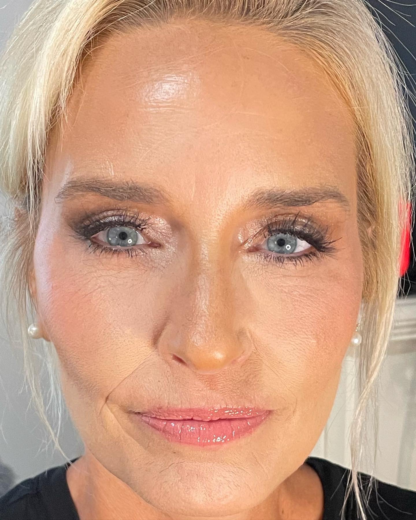 Close-up portrait of a blonde woman with blue eyes, makeup, and pearl earrings.