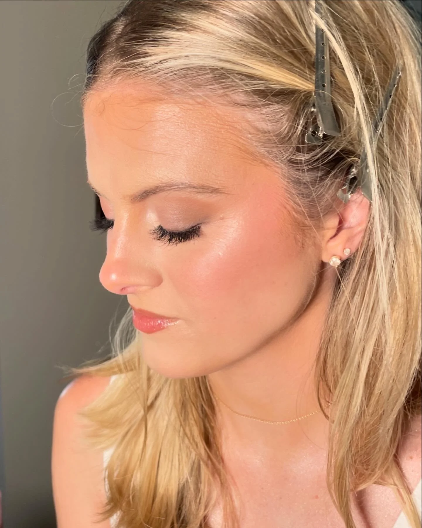 Close-up of a woman with blonde hair, closed eyes, wearing pearl earrings, and clipped hair with metallic hairpins, with a neutral background.