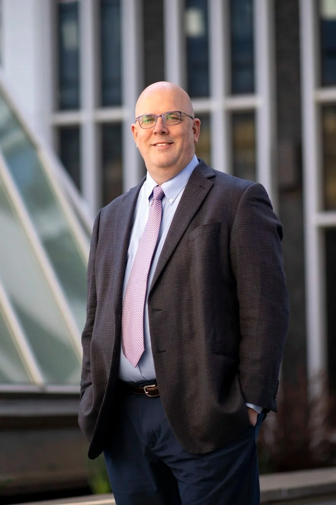 Dr. Shawn Bushway, Chief Scientist, standing outdoors in front of modern glass and metal building, wearing a suit and glasses, smiling.