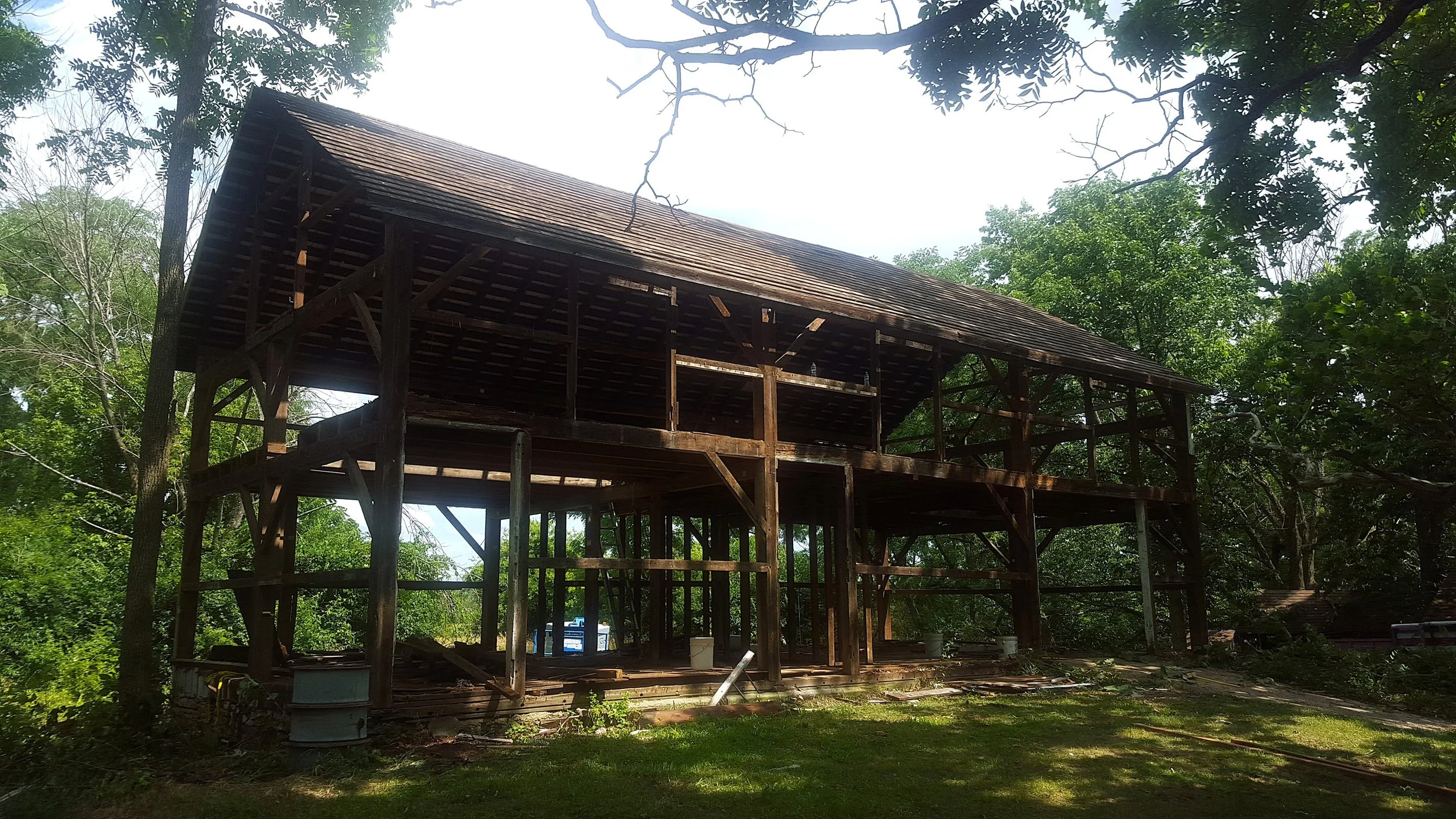 Wooden house under construction surrounded by trees with green leaves.