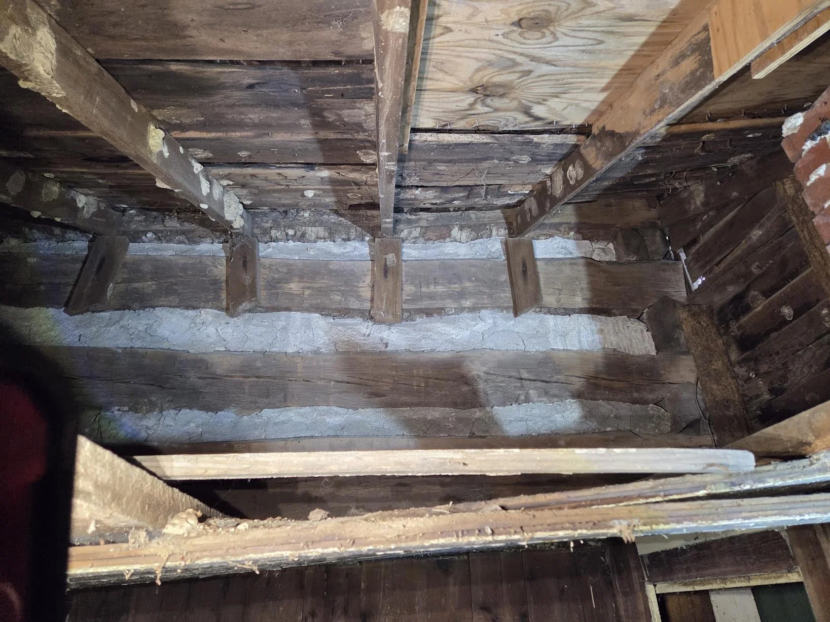 View of an old wooden floor with exposed beams and a layer of concrete or mortar unevenly applied between the wooden planks.