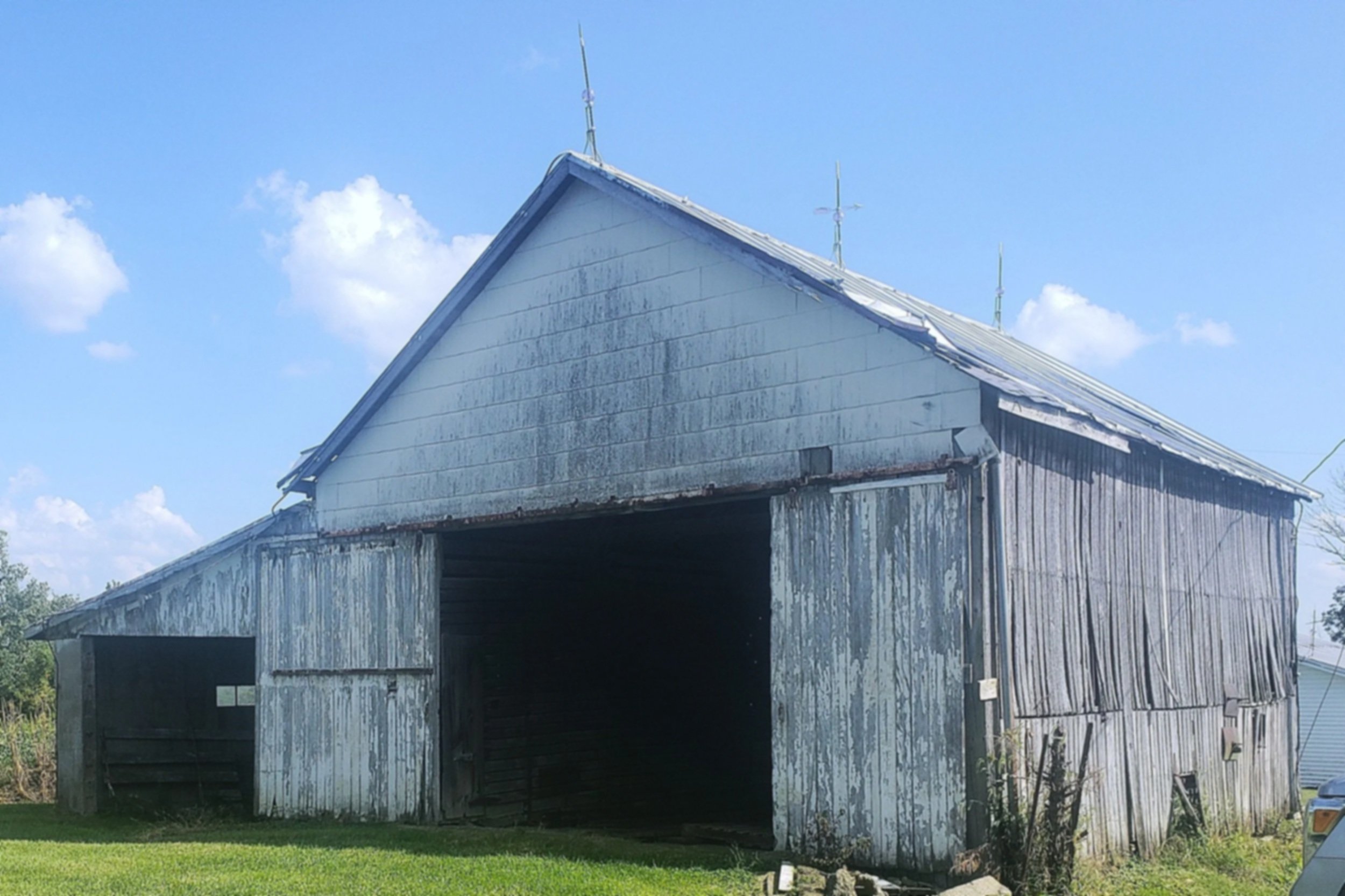 Old, weathered wooden barn under a blue sky with scattered clouds, surrounded by green grass.