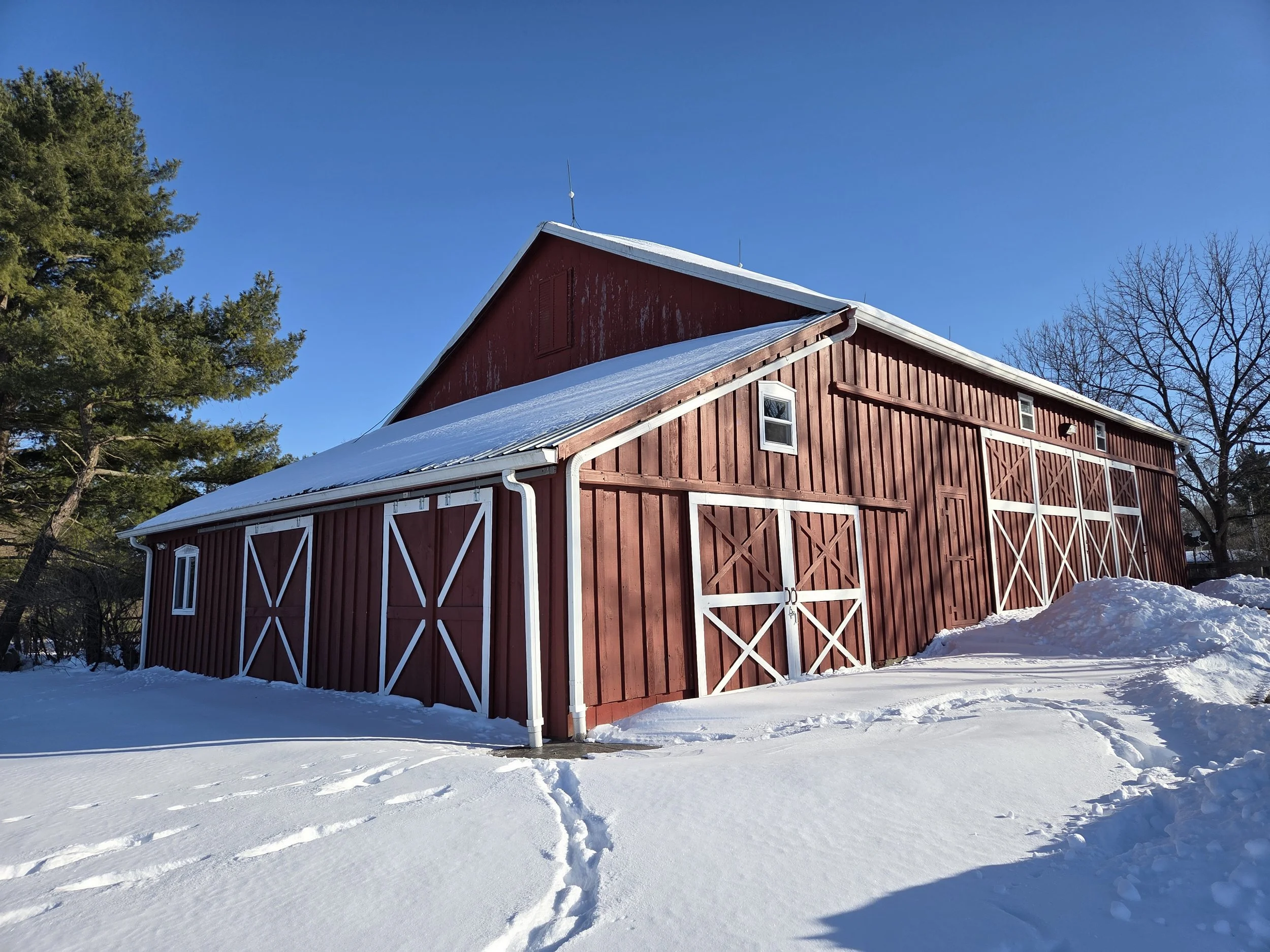 Red barn with white trim covered in snow