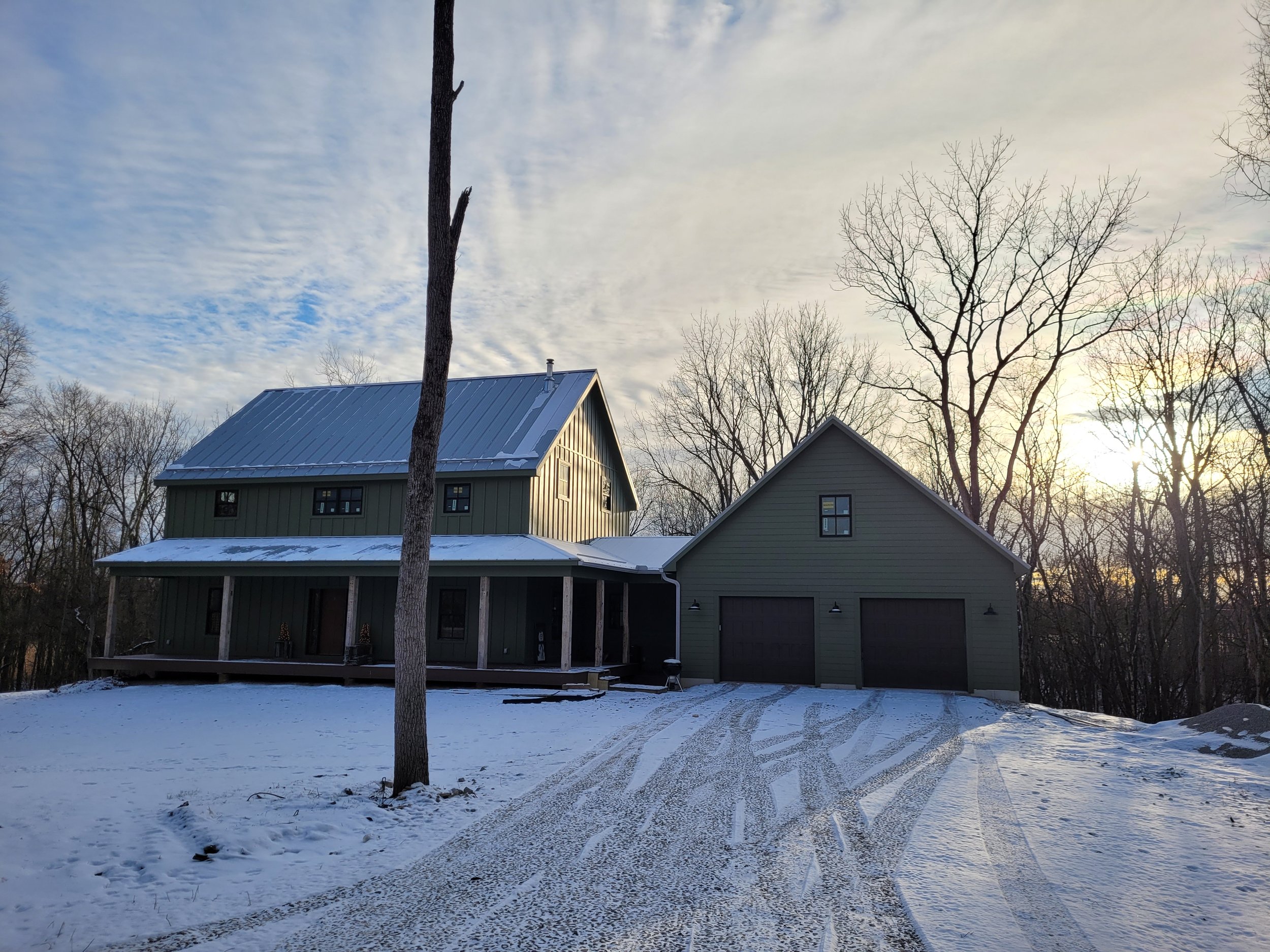 A snowy yard in front of two neighboring houses with bare trees in winter, under a cloudy sky at sunset.