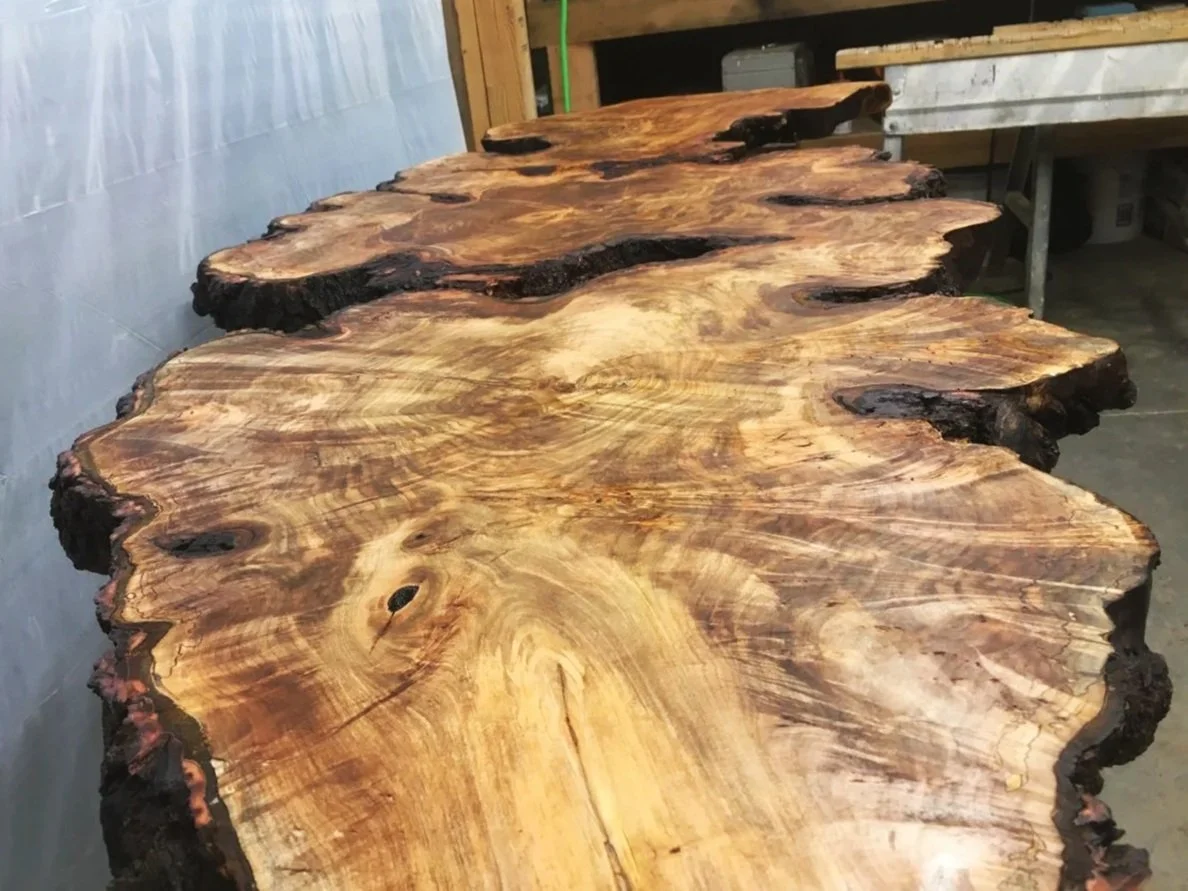 A large rustic wooden table with a live edge design in a woodworking workshop.