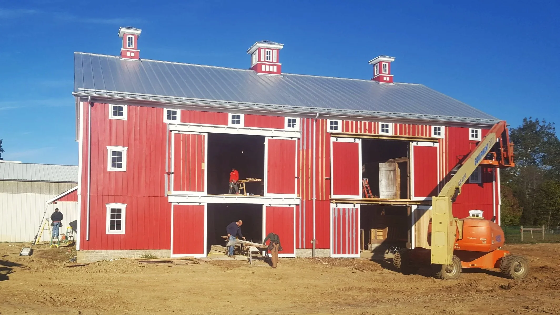 A red barn under construction with workers and equipment on a clear day.