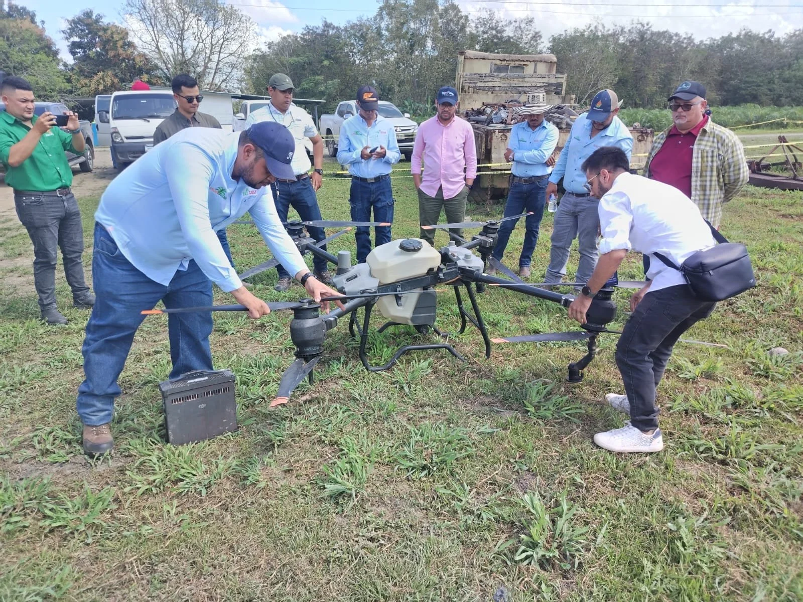 Grupo de personas rodeando un dron en un campo, realizando pruebas o demostraciones.