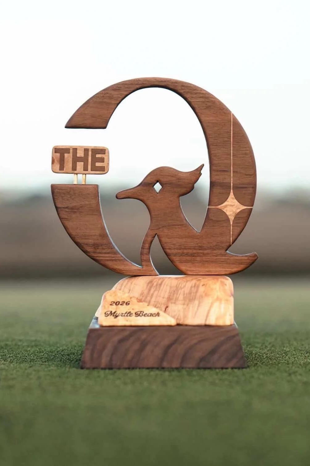 Wooden trophy with the shape of the letter Q, a deer head silhouette, and a sign that says 'THE'. The base reads '2026 Myrtle Beach'.