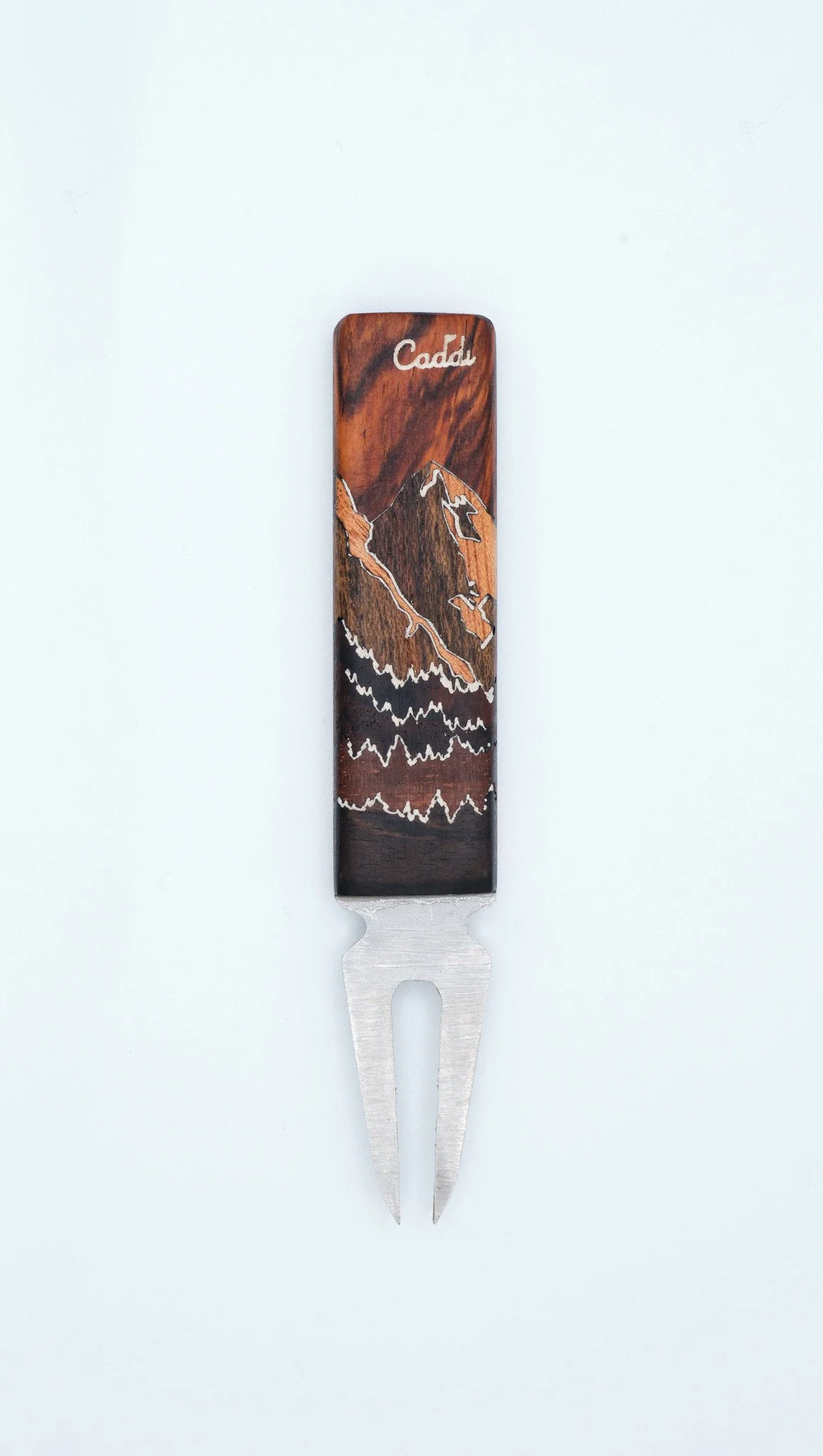 A Luxury Divot tool with a intricate wooden handle featuring a mountain and forest design, with the word 'Caddi' at the top.