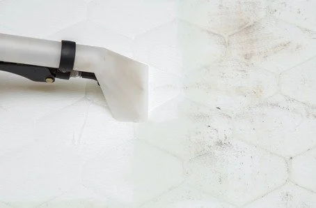 A close-up of a dryer vent pipe extending from a wall with dust around the opening.