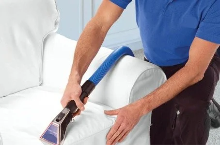 A person cleaning a white couch with a handheld vacuum cleaner.